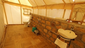 Un baño con tienda de campaña, inodoro, lavabo y pared de piedra.