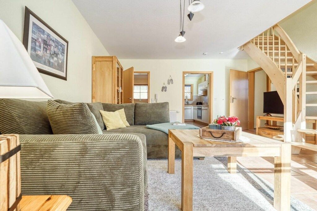 A living room with a sofa, a coffee table, and a TV. There is a staircase leading to another level.
