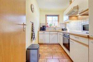 A compact kitchen with a window, a dishwasher, a stove, and a trash bin. - 4.4/T3 holiday home park “Freesenbruch” (Zingst (Ostseeheilbad))