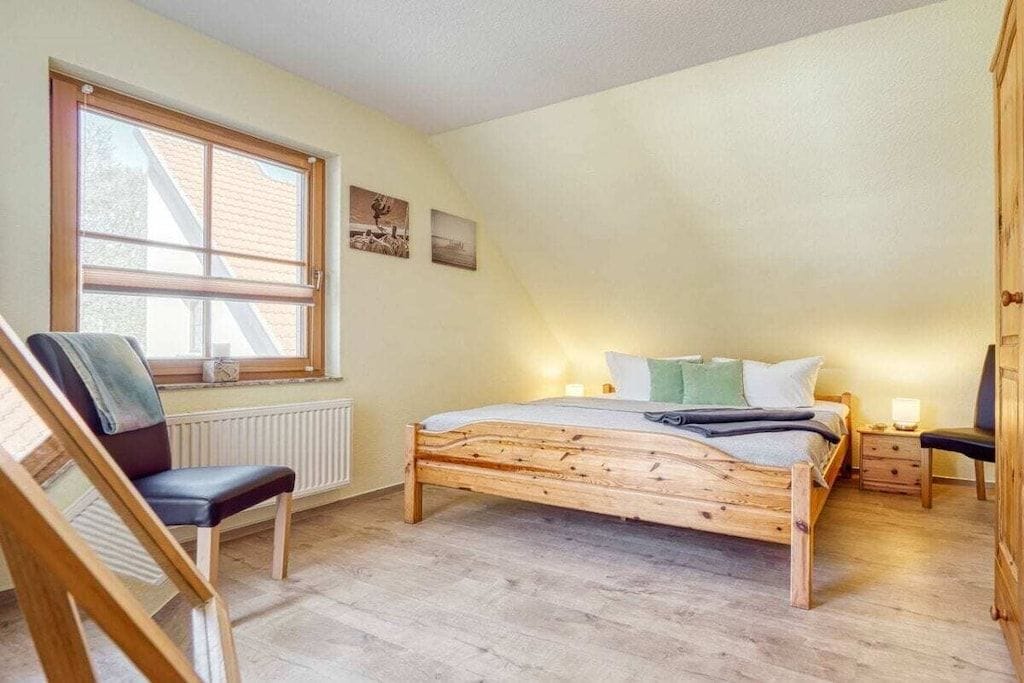Un dormitorio con techo inclinado, una cama de madera, una silla, una mesita de noche y un ventanal.