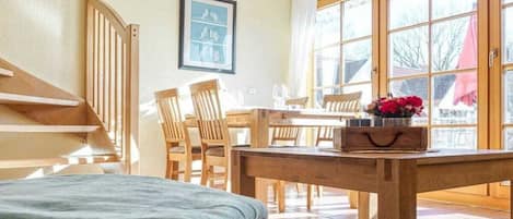 Quarto com uma cama, uma mesa de madeira com cadeiras, uma janela com cortinas e um lustre.