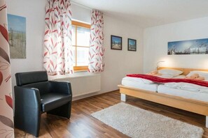 Een slaapkamer met een bed, een stoel, een radiator en een raam met gordijnen.