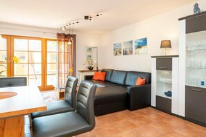A modern living room with a black leather sofa, a dining table, and a glass cabinet. - 3.1/T4 holiday home park “Freesenbruch” (Zingst (Ostseeheilbad))