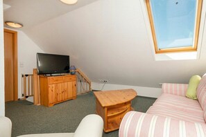 A small, cozy room with a sloped ceiling, a television on a wooden cabinet, a small wooden stool, and a striped sofa with pillows. - 2.5/T3 holiday home park “Freesenbruch” (Zingst (Ostseeheilbad))