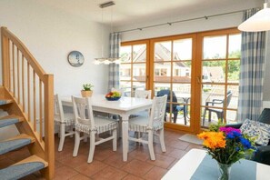 A dining area with a white table and chairs, a potted plant, and a vase with flowers. - 2.5/T3 holiday home park “Freesenbruch” (Zingst (Ostseeheilbad))