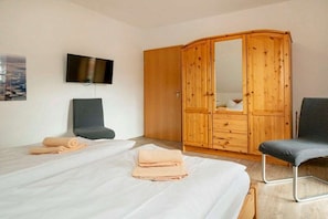 Ein Schlafzimmer mit einem Bett, zwei Stühlen, einem Kleiderschrank, einem Fernseher und einem Gemälde an der Wand.