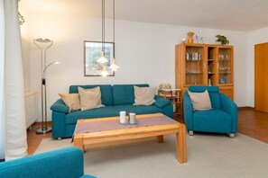 Ein Wohnzimmer mit einem petrolfarbenen Sofa, einem passenden Sessel, einem Holztisch und einer Stehlampe.