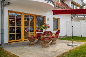 A patio with wicker chairs and a table, a red umbrella, and a white fence in the background. - 1.2/T4 holiday home park “Freesenbruch” (Zingst (Ostseeheilbad))
