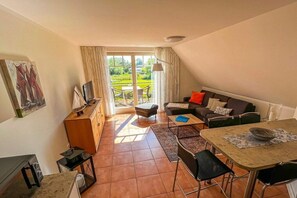 A cozy living area with a sofa, a dining table, and a view of a garden through a glass door. - Mühlenstraße 19 Apartment 4 (Seeheilbad Zingst)