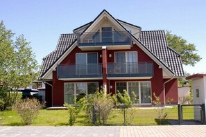 A two-story residential building with a balcony on the upper floor, a fenced yard, and a clear sky. - Mühlenstraße 19 Apartment 4 (Seeheilbad Zingst)