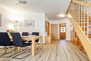 A dining area with a wooden table and chairs, a hanging light fixture, and a staircase with wooden railings. - 6a/T5 in the "Freesenbruch" holiday park (Zingst (Ostseeheilbad))