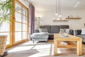 A modern living room with a sofa set, a coffee table, and a large window with curtains. - 6a/T5 in the "Freesenbruch" holiday park (Zingst (Ostseeheilbad))