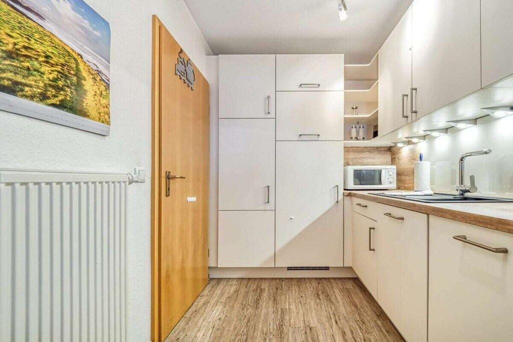 Une cuisine de taille réduite avec des meubles blancs, un four à micro-ondes et une porte en bois.