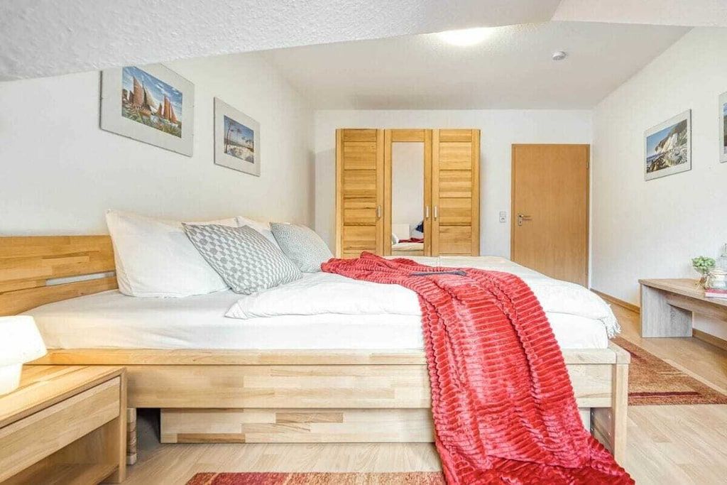 A bedroom with a wooden bed, a nightstand, a red blanket, and a wardrobe with a mirror.