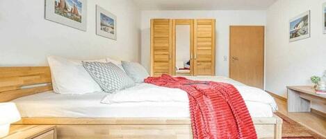A bedroom with a wooden bed, a nightstand, a red blanket, and a wardrobe with a mirror.