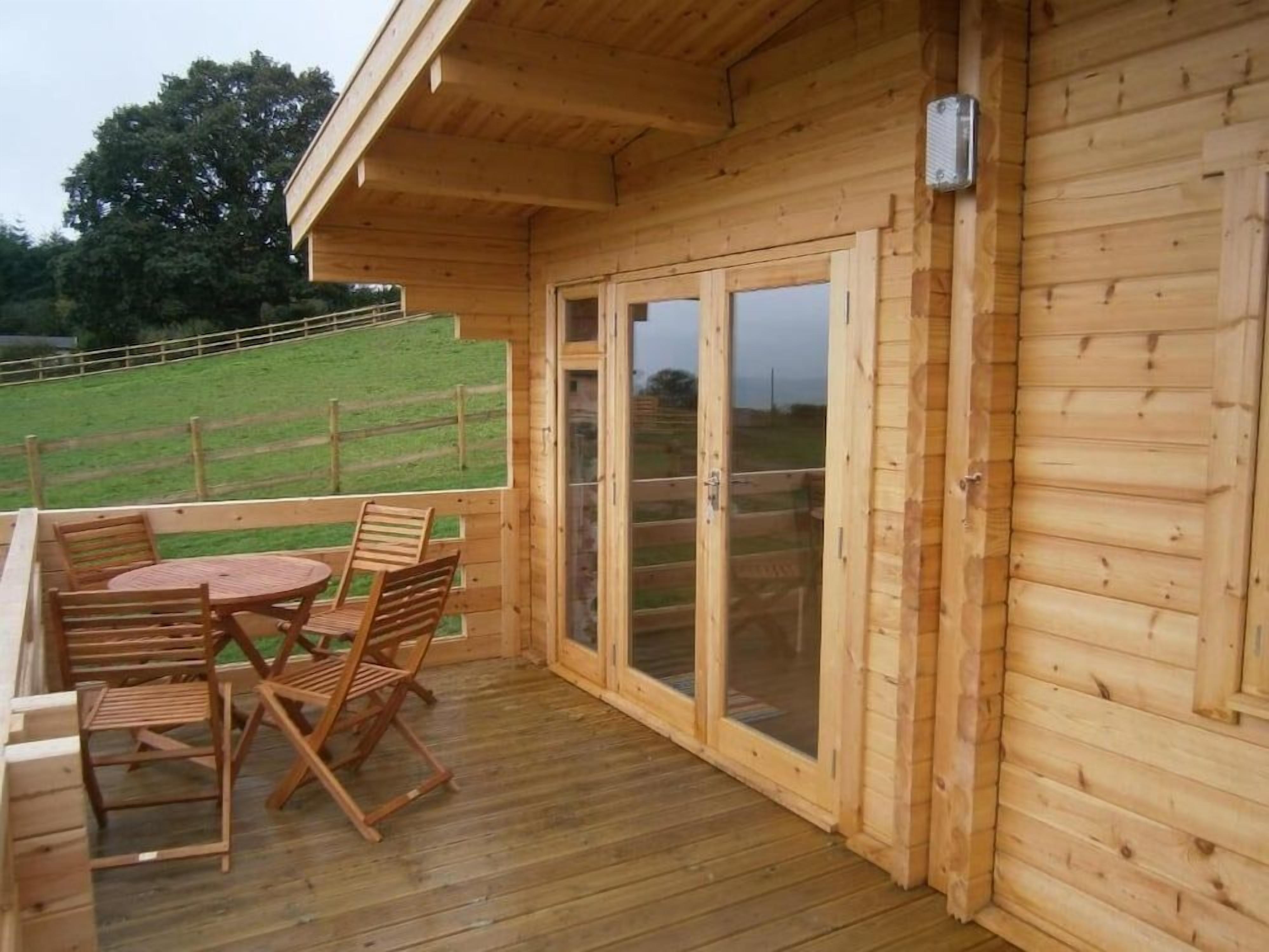 A wooden deck with a table and chairs, a sliding glass door, and a view of a grassy area.