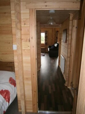 A narrow hallway with wooden walls and a bed with a red heart pattern on the left.