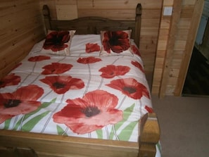 A wooden bed with a poppy-patterned bedspread and pillows.