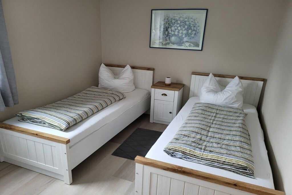 A bedroom with two single beds, a nightstand, a framed picture on the wall, and a dark rug on the floor.