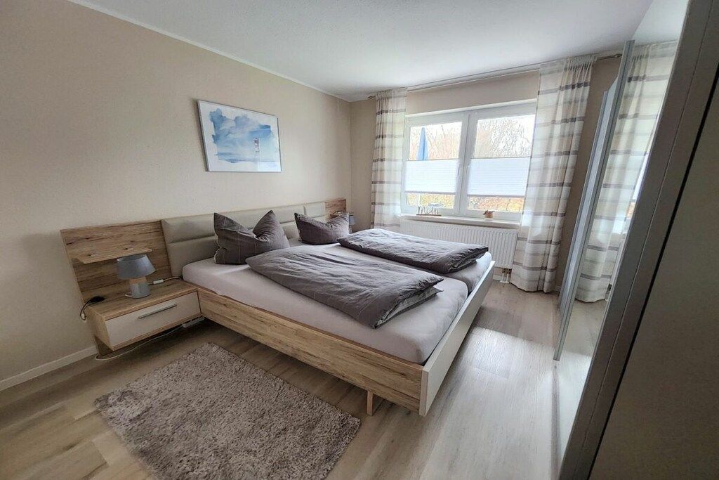 A bedroom with a bed, bedside tables, a lamp, a window with curtains, and a painting on the wall.