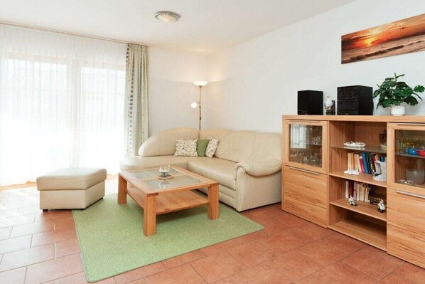 A living room with a sofa, a coffee table, a bookshelf, and a lamp. - 2.2/T4 holiday home park “Freesenbruch” (Zingst (Ostseeheilbad))