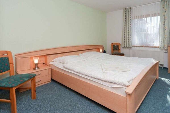 A single bed with a wooden headboard, a bedside table with a lamp, and a chair with a cushion. - 2.2/T4 holiday home park “Freesenbruch” (Zingst (Ostseeheilbad))
