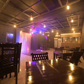 Un espacio interior amplio con mesas, sillas, una pantalla de proyección mostrando un mapa y una zona de bar con taburetes.