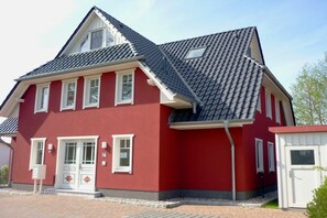 Ein rotes Haus mit grauem Dach, weißen Fenstern und einer kleinen angebauten Garage.