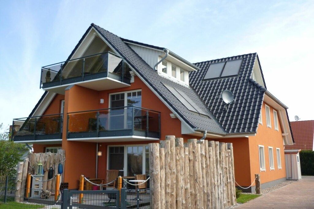 Ein zweistöckiges Haus mit Balkon, umzäunter Garten und blauem Himmel.