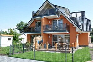 Ein zweistöckiges Wohngebäude mit Balkon, umzäunter Garten und einer kleinen Spielgegend.
