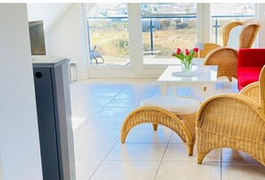 A bright room with wicker furniture, a white table, and a view through a large window. - Holiday apartment Mühlenstr. 19/5 Sun deck (Seeheilbad Zingst)