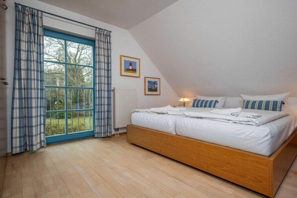 Ein Schlafzimmer mit großem Fenster, einem Bett und zwei gerahmten Bildern an der Wand.