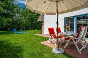 Eine Terrasse im Freien mit Tisch und Stühlen, einem Rasen und einem Gebäude mit einer blauen Tür.