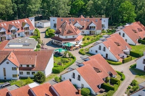Ein Wohngebiet mit mehreren Häusern, die rote Ziegeldächer und weiße Fassaden haben, umgeben von viel Grün.