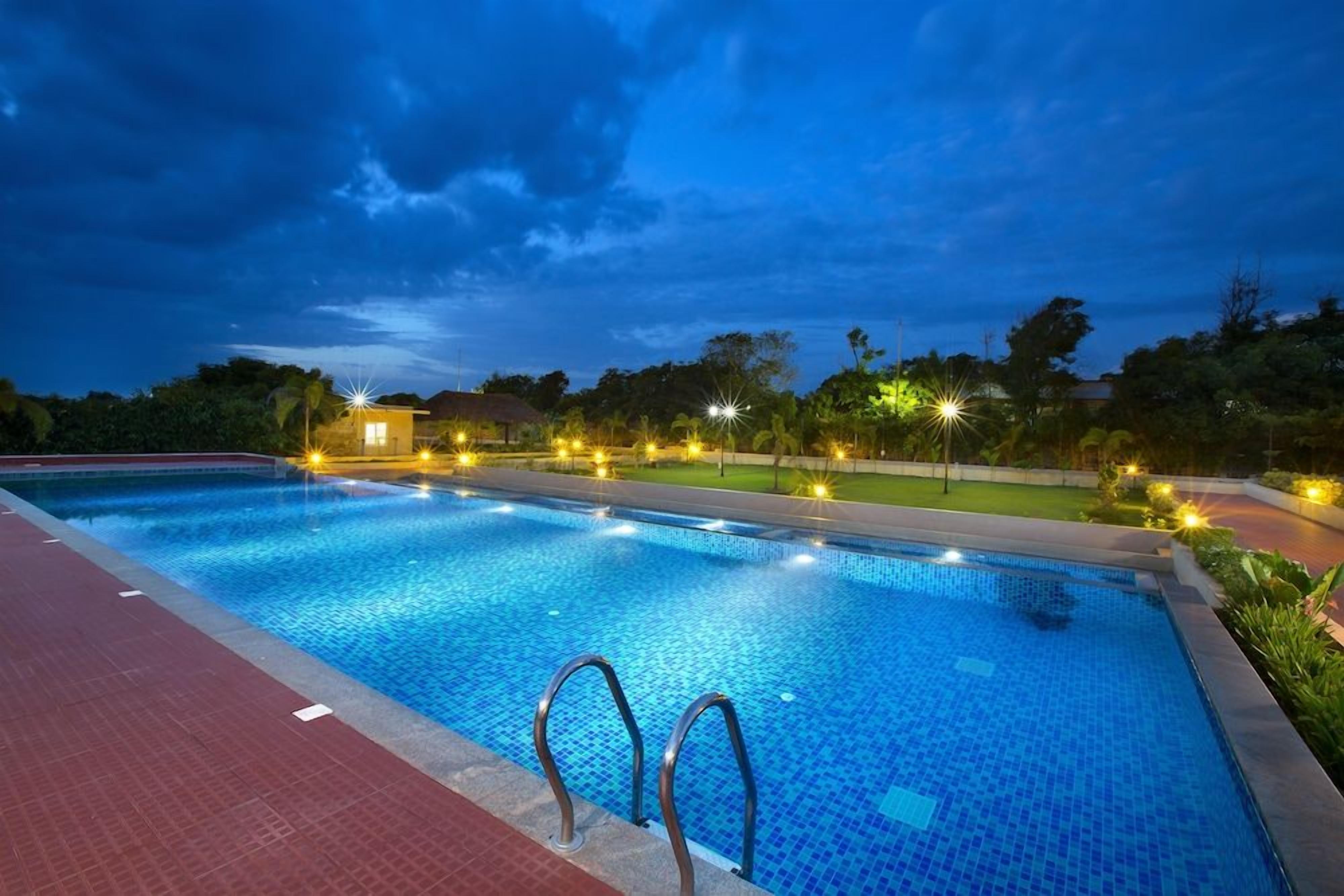 A swimming pool with a tiled edge, surrounded by a paved walkway, and illuminated by overhead lights.