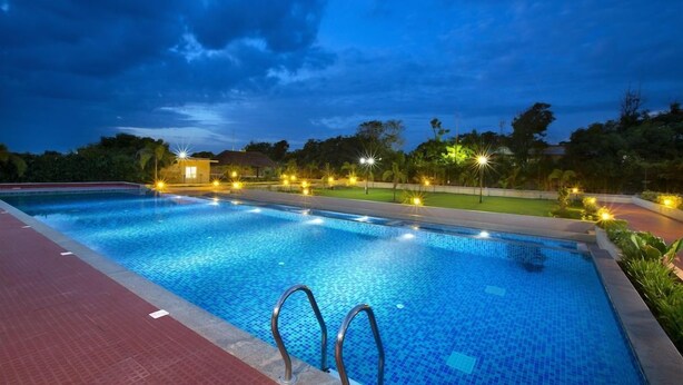 Piscina com borda azulejada, rodeada por um calçadão pavimentado e iluminada por luzes no teto.