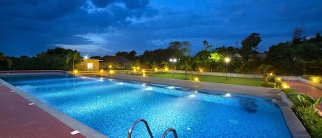 A swimming pool with a tiled edge, surrounded by a paved walkway, and illuminated by overhead lights.