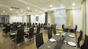 Sala de conferência com várias mesas e cadeiras, ventiladores de teto e iluminação embutida.