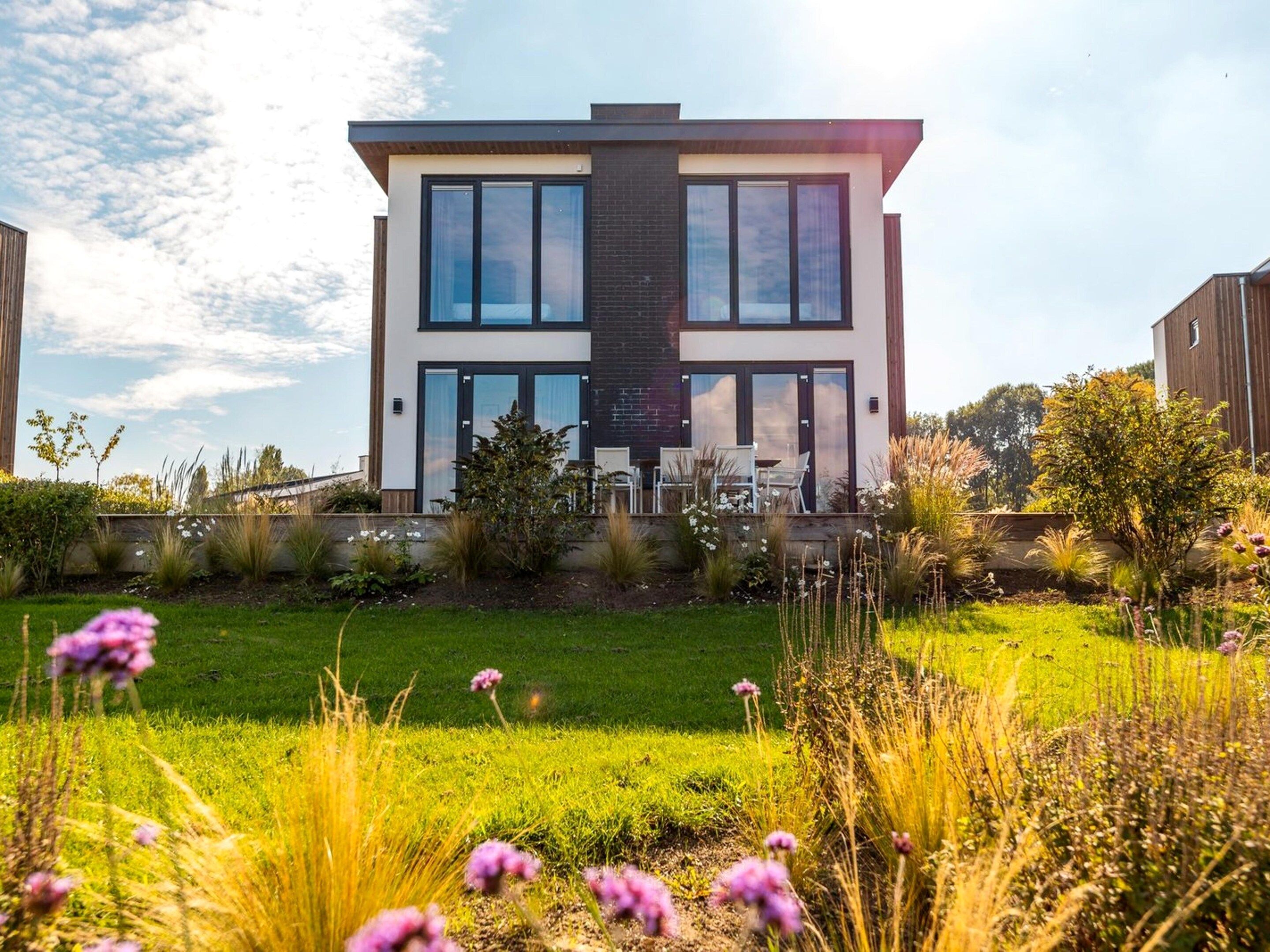 A modern two-story house with a flat roof, large windows, and a well-maintained garden in front.