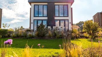 A modern two-story house with a flat roof, large windows, and a well-maintained garden in front.