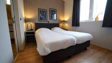 A hotel room with a double bed, two bedside lamps, a window with curtains, and a wooden floor.