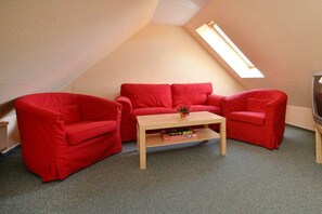 A room with a sloped ceiling, a red sofa set, a wooden coffee table, and a television. - 1.6/T1 holiday home park “Freesenbruch” (Zingst (Ostseeheilbad))