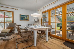 A dining area with a white table and chairs, a pendant light, and a view of the outdoors through large glass doors. - 6/T5 holiday home park “Freesenbruch” (Zingst (Ostseeheilbad))