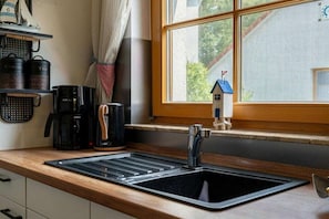 Ett kök med en svart diskho, en kaffebryggare och ett fönster med utsikt över ett hus.