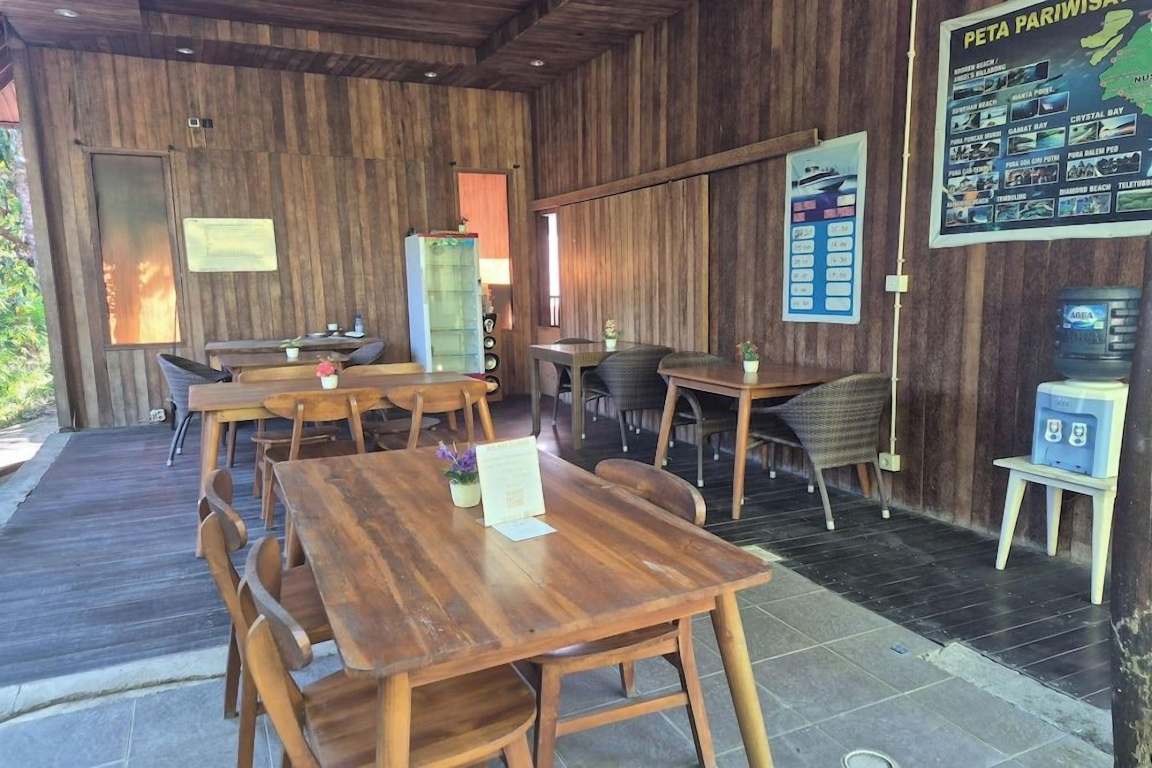 Un interior de madera con varias mesas y sillas de comedor, un refrigerador y una pizarra con el menú.