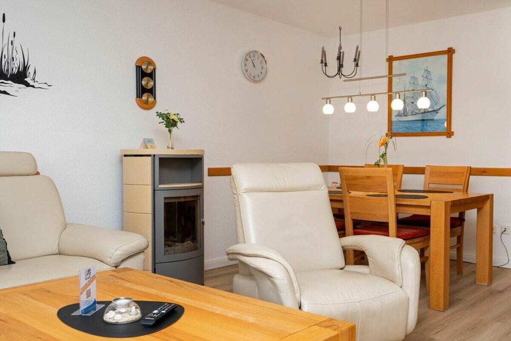 A modern living room with a fireplace, leather chairs, a wooden dining table, and a chandelier.