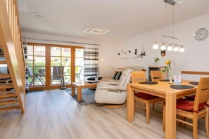A modern living room with a sofa, a dining table with chairs, a staircase, and a large window with curtains. - 5a/T5 in the "Freesenbruch" holiday park (Zingst (Ostseeheilbad))