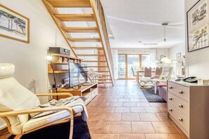 A spacious living area with a high ceiling, a staircase, and a view through glass doors to an outdoor patio. - 7a/T5 in the holiday apartment park "Freesenbruch" (Zingst (Ostseeheilbad))