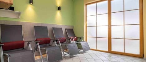 Una habitación con una fila de sillones de masaje, un ventanal con vidrio esmerilado y una pared verde.