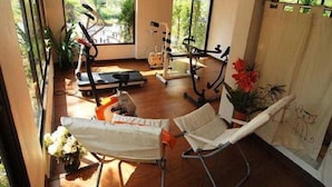 Una habitación con piso de madera, equipo de ejercicio, una silla blanca y una ventana con vistas a follaje.